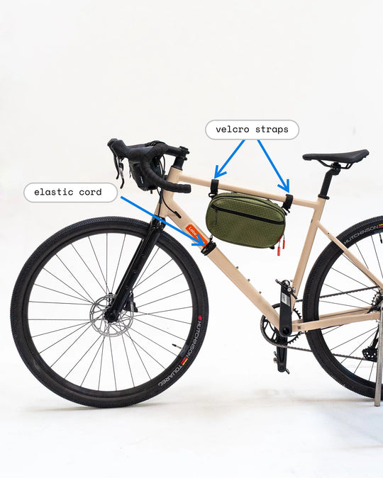 Sling bag carried inside the bike frame — velcro straps on the top tube, elastic frame cord anchoring the base to the down tube