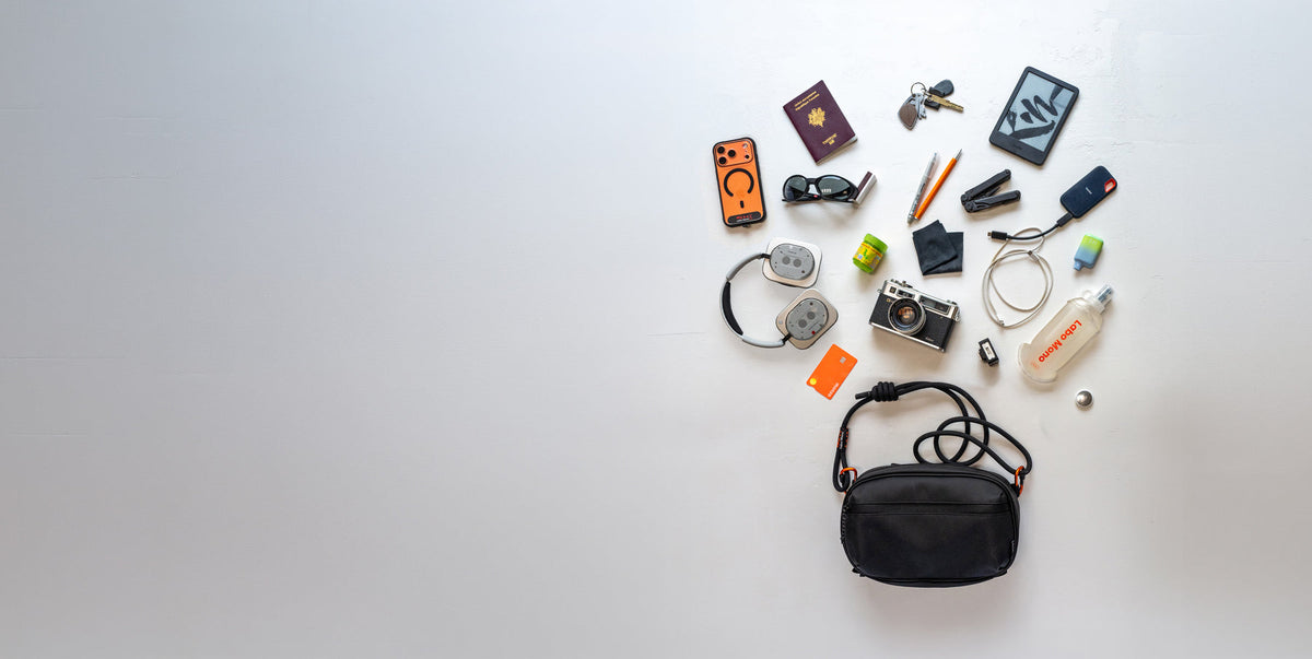 The Labo Mono sling bag with a phone, passport, keys, Kindle, camera and headphones laid out above it